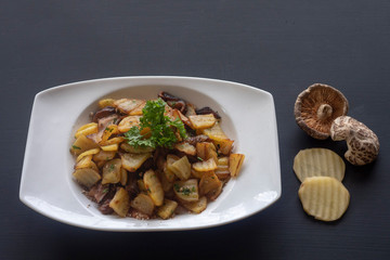 fried potatoes with mushrooms on a white plate on a dark background