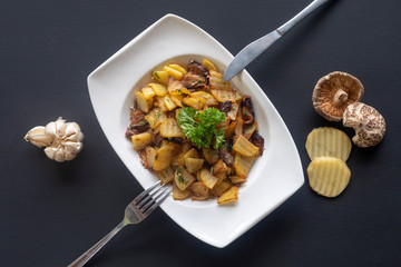 fried potatoes with mushrooms on a white plate on a dark background