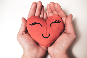 Obraz premium Kawaii heart in hands on a white background. Drawing the eyes and mouth on the heart