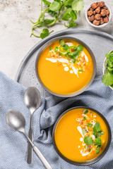 Pumpkin soup in bowl garnished with cream, hazelnut and watercress. Top view. Comfort food. Cream of pumpkin squash soup