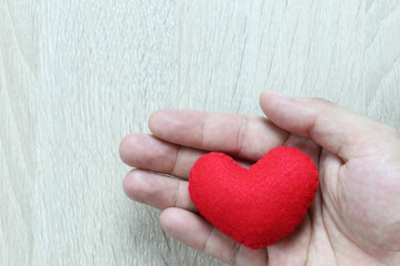Red heart in hand on wooden floor and have copy space for design in your work concept.