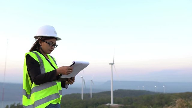 women engineer working and holding the report at wind turbine farm Power Generator Station on mountain,Thailand people
