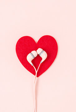 Earphone with red heart on pink background.