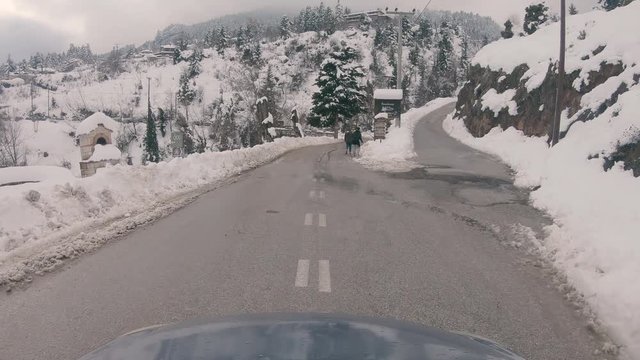 Driving through Trikala Corinthia, people walking on the road. Cars parked around blocking the road. Winter day with a lot of snow causing a traffic jam on the main road of the village.