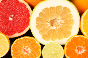 cut pieces of different citrus fruits on dark background