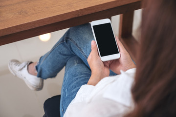Mockup image of a woman holding white mobile phone with blank screen while sitting in cafe