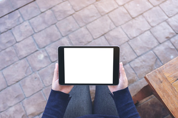 Top view mockup image of a woman holding black tablet pc with blank white screen horizontally while sitting in the outdoors