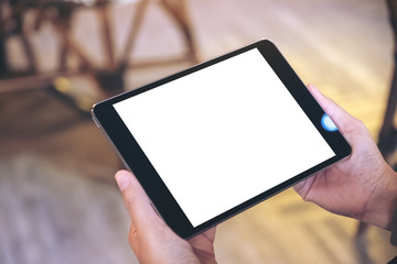 Mockup image of a woman holding black tablet pc with blank white screen horizontally while sitting in cafe