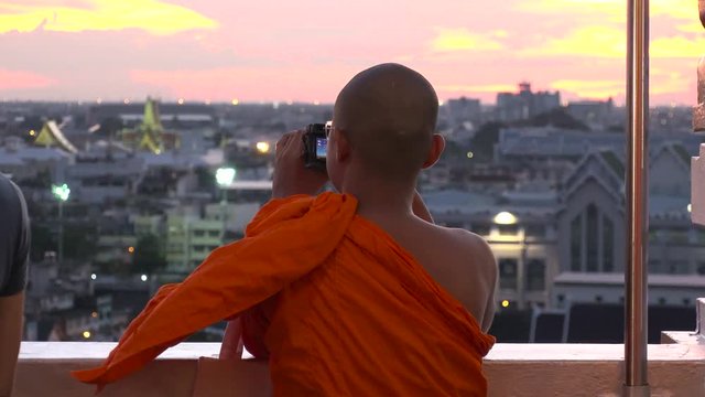 BANGKOK,  THAILAND - CIRCA OCTOBER 2018 : Back shot of unidentified MONK taking photo of CITYSCAPE of BANGKOK from above in SUNSET TIME.  Located at WAT SAKET.