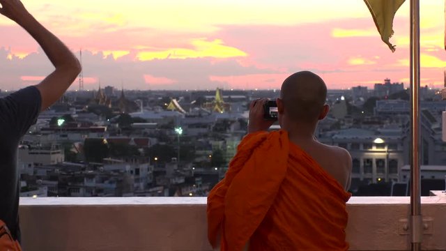 BANGKOK,  THAILAND - CIRCA OCTOBER 2018 : Back shot of unidentified MONK taking photo of CITYSCAPE of BANGKOK from above in SUNSET TIME.  Located at WAT SAKET.