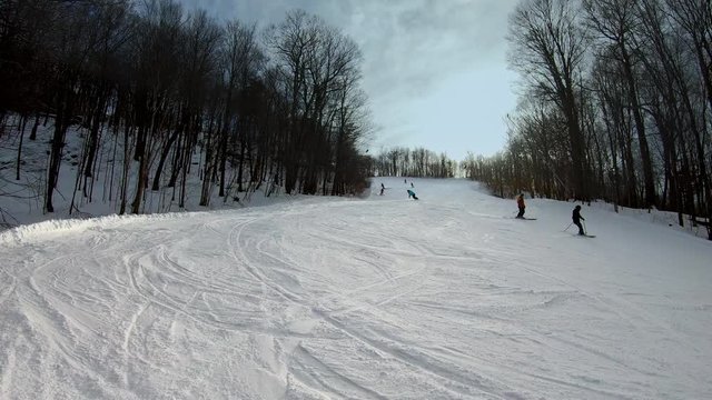 Skiers and snowboarders going down the slope and making turns. People having fun skiing and snowboarding on a groomed trail. Beautiful Vermont winter vacation. Wide shot.