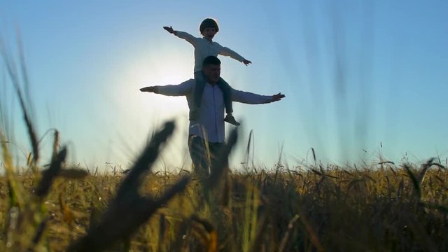 silhouette of father and son playing, airplane arms raised together at sunset in wheat field, happy family walking outdoors. child boy having fun, rising up hands, travel, holiday flight nature summer