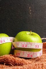 HEALTH LIFESTYLE CONCEPT: Green apples and measuring tape over black rustic background. Selective focus.