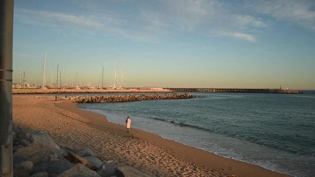 Walking next to the beach in the sunset with beautiful light. You see a woman near the sea.