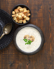 Champignon mushroom cream soup in bowl on wooden background. Rustic style. Top view.