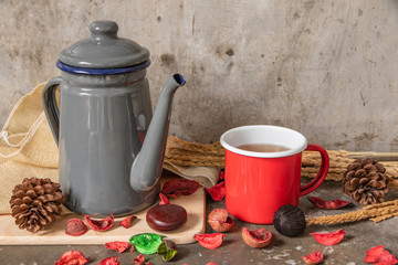 Gray metal teapot and red tin cup on cement table background.