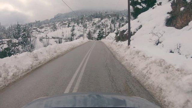 Driving through Trikala Corinthia, people walking on the road. Cars parked around blocking the road. Winter day with a lot of snow causing a traffic jam on the main road of the village.