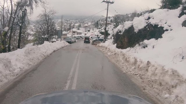Driving through Trikala Corinthia, people walking on the road. Cars parked around blocking the road. Winter day with a lot of snow causing a traffic jam on the main road of the village.