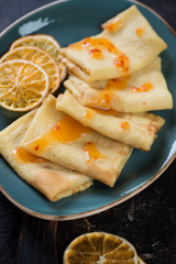 Crepes with orange sauce and orange fruit chips served on a turquoise plate, vertical shot, close-up