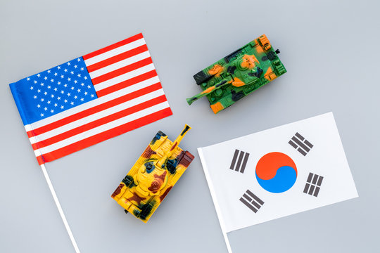 War, confrontation concept. Korea, USA. Tanks toy near korean and american flag on grey background top view