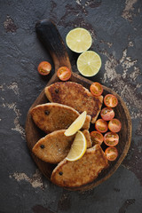 Roasted fish cutlets with cherry tomatoes, lemon and lime. Top view on a brown stone background, vertical shot