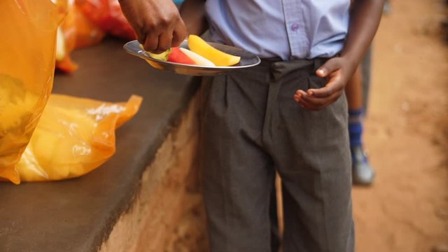 Rural African school pupil steps forward to receive fresh cut fruit in tin plate for lunch