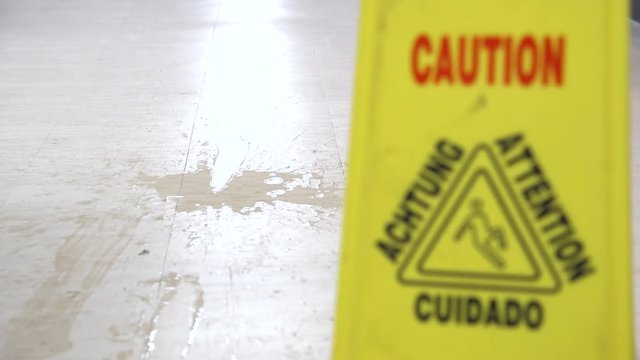A man slipping on a wet floor in front of a caution slippery sign.