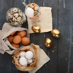 Quail eggs in glass container, white in paper and yellow in canvas bag and gold eggs on wooden background.