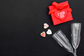 Valentine's day dinner concept. Wine glass and gift box on black background top view copy space