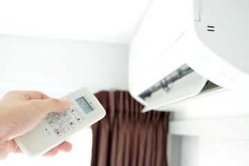 Man's hand using remote control open The air conditioner is cooled to 25 degrees Celsius in his bedroom. Health concepts and energy savings