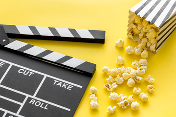 Movie premiere concept. Clapperboard and popcorn on yellow background