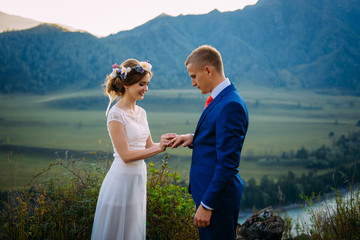 Newlyweds on wedding ceremony on background of mountains. The bride is dressed in classic white wedding dress, the groom is wearing in suit with a red tie