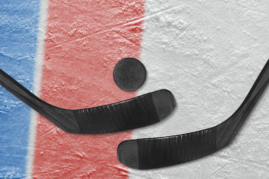 Blue and red lines on the ice, and two hockey sticks with the puck