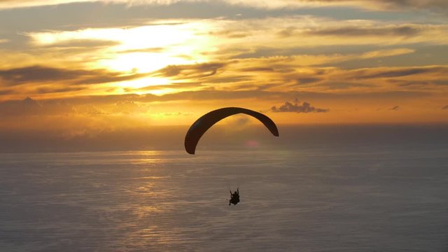 Paraglider navigates his way across golden sky as sun sets over the ocean