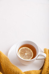 White cup of tea with lemon on a saucer on white background with a cozy orange sweater. Copy space. Flat lay