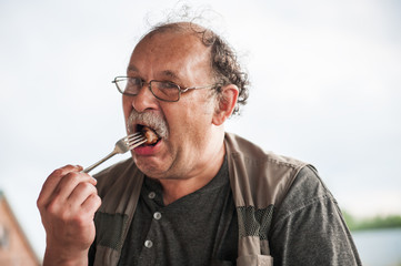 Adult man with glasses and a mustache puts in his mouth a piece of meat