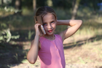 on the background of nature a little girl emotionally talking on the phone with a friend