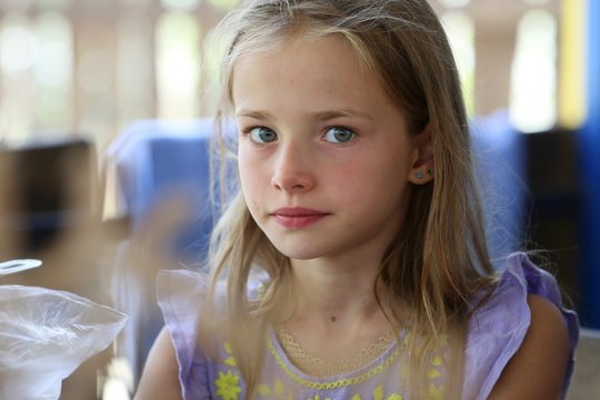 Portrait of a little girl with long hair and blue eyes of a blonde who is resting in nature, is seriously looking at the camera closeup