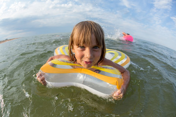 portrait, happy little girl swims in the sea on an inflatable circle, wide-angle landscape