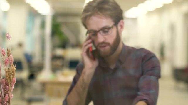 Bearded smiling guy with glasses and casual plaid shirt talking on a cell phone.