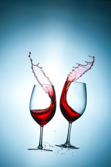 Two Glasses with Red Wine Splashes Poured Out from Glasses Against Bluish Background. Short Flash Duration for Freezing Motion Used. Vertical Image Composition