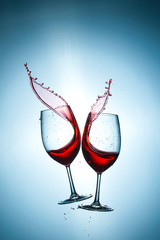 Two Glasses with Red Wine Splashes Poured Out from Glasses Against Bluish Background. Short Flash Duration for Freezing Motion Used. Vertical Image Composition