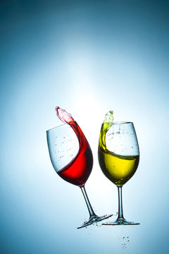 Two Types of Colorful Red and Light Yellow Wine Splashes Poured Out from Glasses Against Bluish Background. Short Flash Duration for Freezing Motion Used. Vertical Image Orientation