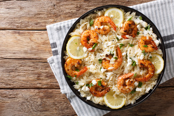 Mediterranean food Pasta orzo with grilled shrimps, feta cheese and lemon close-up on a plate. Horizontal top view