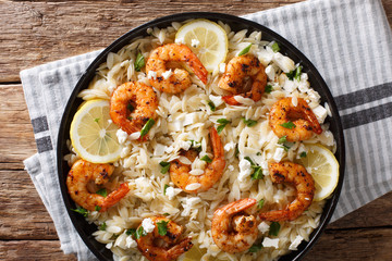 Orzo pasta with grilled shrimps, feta cheese and lemon close-up on a plate. horizontal top view
