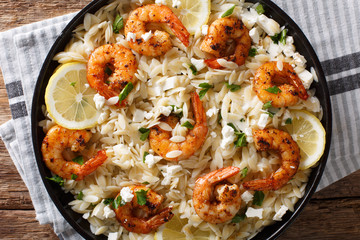 Italian pasta orzo with grilled shrimps, feta cheese and lemon closeup on a plate. Horizontal top view