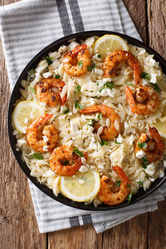 Orzo pasta with grilled shrimps, feta cheese and lemon close-up on a plate. Vertical top view