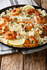 Italian pasta orzo with grilled shrimps, feta cheese and lemon closeup on a plate. vertical