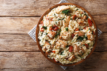 Italian pasta orzo with grilled chicken, dried tomatoes, spinach and cheese close-up. horizontal top view - obrazy, fototapety, plakaty