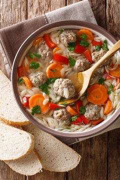 Delicious Italian soup with orzo pasta, meatballs and vegetables close-up on the table. Vertical top view, rustic